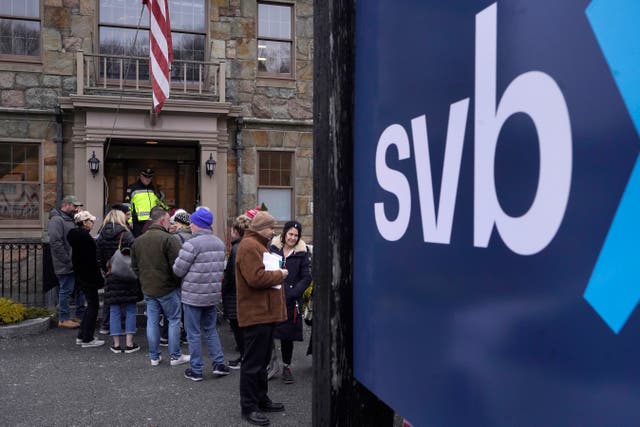 A law enforcement official stands in an entryway to a Silicon Valley Bank branch   as customers and bystanders line up outside the bank, in Wellesley, Massachusetts 