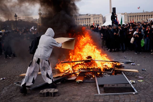 A protester throws cardboard to feed burning pallets during a demonstration at Concorde square near the National Assembly in Paris