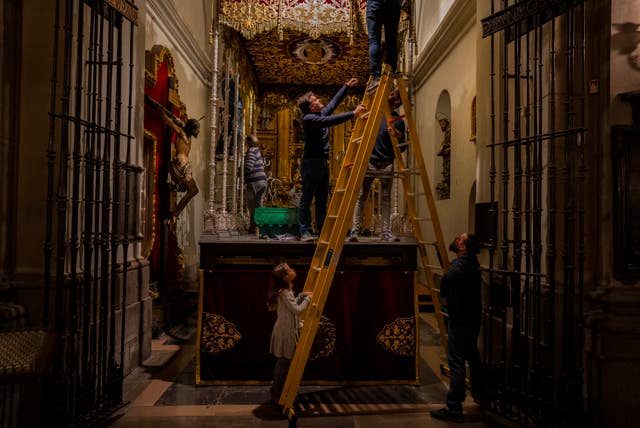 Miembros de la hermandad 'Nustro Padre Jesús del Gran Poder y la Esperanza Macarena' preparan una carroza para llevar una imagen religiosa durante las procesiones de Semana Santa en el interior de una iglesia en Madrid.