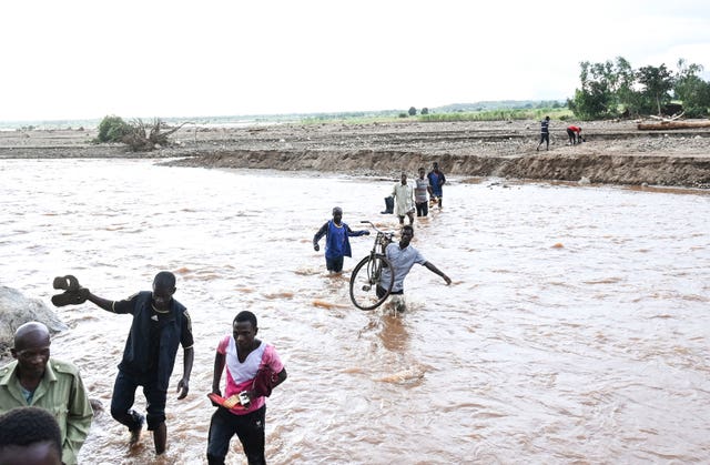 People wade through flood waters caused by last week’s heavy rains caused by Tropical Cyclone Freddy in Phalombe, southern Malawi on March 18, 2023