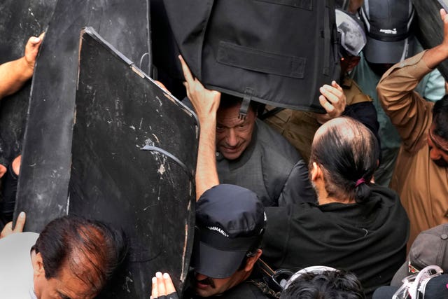 Security personnel hold bulletproof shields to secure former prime minister Imran Khan, centre