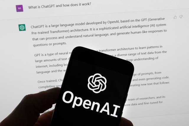 The OpenAI logo on a mobile phone in front of a computer screen which displays output from ChatGPT