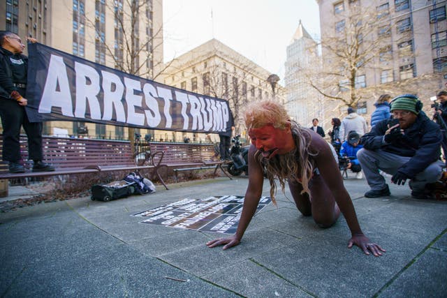 A woman performs with a mask of former president Donald Trump as a small group of people protest near the District Attorney office on Tuesday in New York, in an anticipation of former president’s possible indictment.