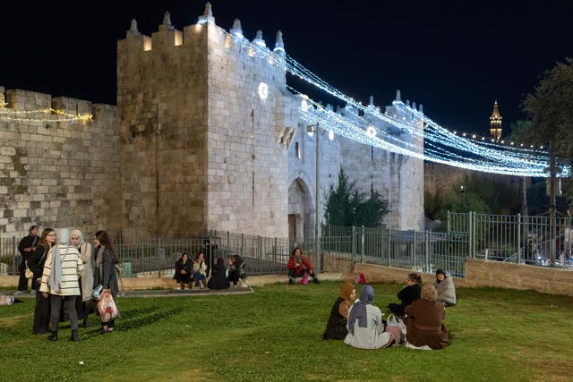 Palestinians sit together next to Damascus Gate decorated with lights at the beginning of Ramadan, just outside Jerusalem’s Old City