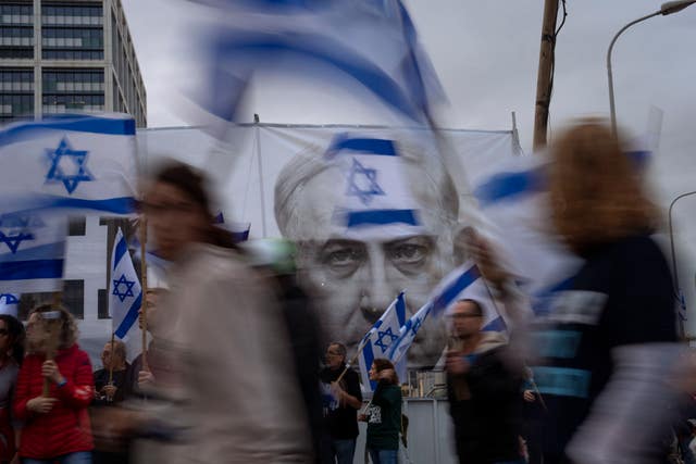 Demonstrators walk with Israel’s national flag next to a banner showing Prime Minister Benjamin Netanyahu during a protest  in Tel Aviv against plans by his government to overhaul the judicial system 