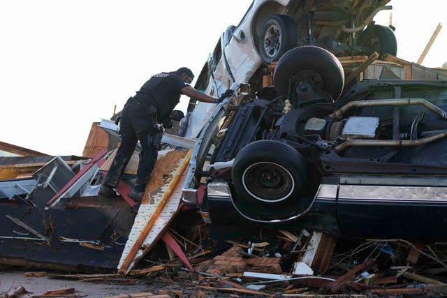 A sheriff’s deputy climbs on a pile of wind-tossed vehicles to search for survivors at Chuck’s Dairy Bar in Rolling Fork 