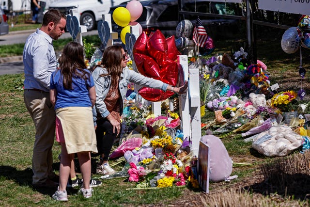 A family pauses at a memorial at the entrance to The Covenant School