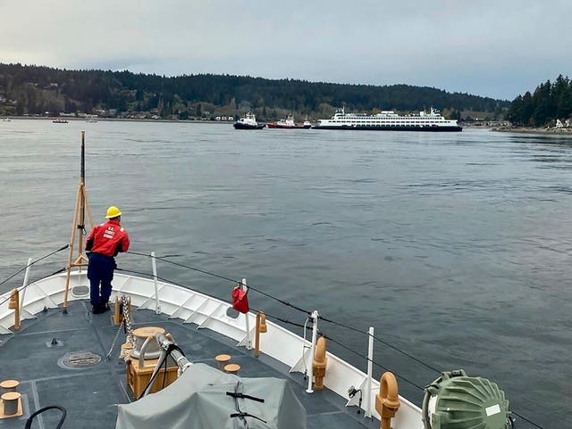 In this photo posted to social media by the US Coast Guard, a crew member stands by ready to assist as emergency personnel respond to the Walla Walla passenger ferry, background right, which ran aground near Bainbridge Island west of Seattle 