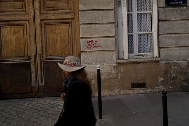 A woman walks past graffiti reading “Emily Not Welcome” scrawled on part of the facade of the building where the fictional character Emily Cooper lives, at 1 Place de d’Estrapade, in Paris
