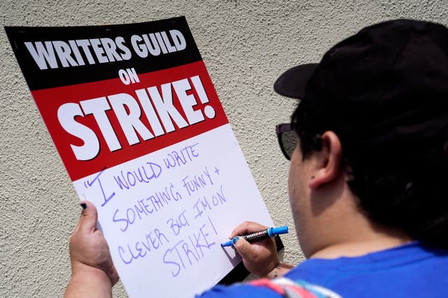 Isaac Gomez, a captain in the Writers Guild of America West, writes out a message on a sign before a rally in front of Paramount Pictures in Los Angeles