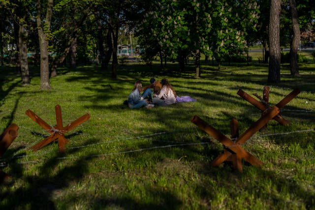 People sit in a park next to anti-tank hedgehogs in Kyiv