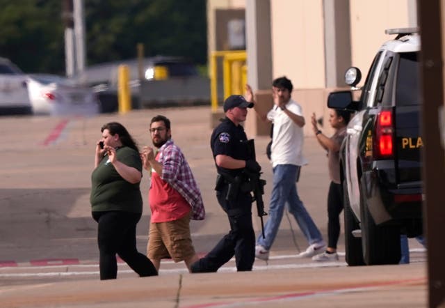 People raise their hands as they leave a shopping center following reports of a shooting in Allen, Texas