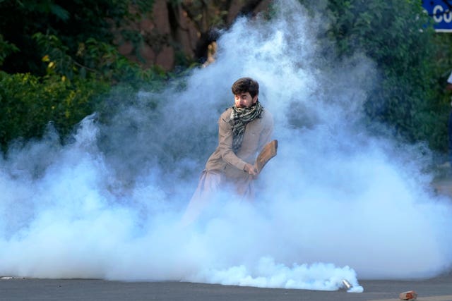 A supporter of Mr Khan removes a tear gas shell fired by police to disperse them protesting against the arrest of their leader 