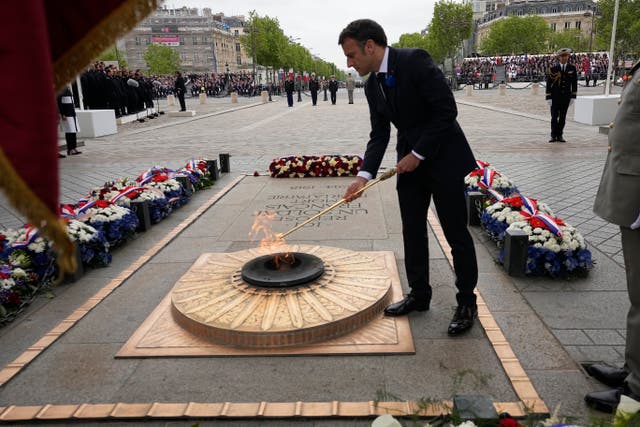 French President Emmanuel Macron revives the flame at the Unkown Soldier tomb under the Arc de de Triomphe during ceremonies marking Victory Day in Paris