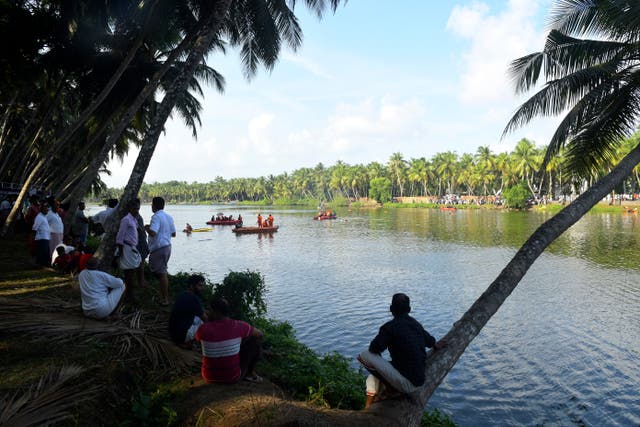 People watch rescuers search a river after a tourist boat capsized in Malappuram, Kerala, India 