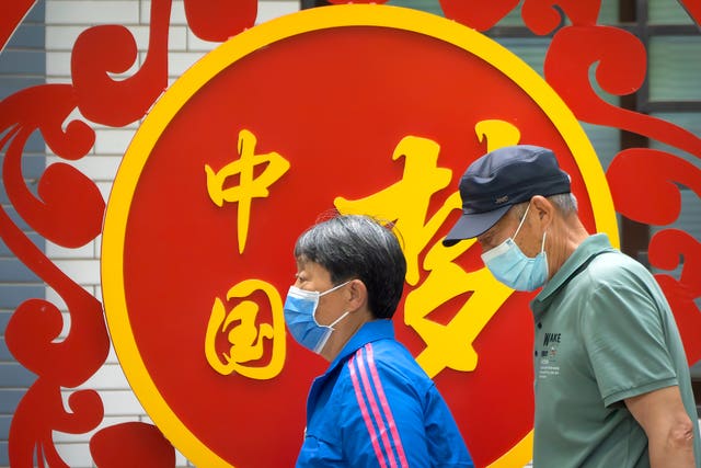 People wearing face masks walk past a billboard reading “China Dream” at a public park in Beijing