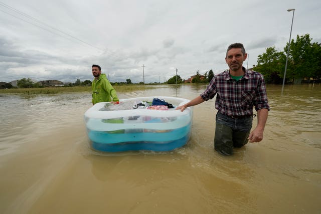 People use a plastic portable pool to carry bags and personal effects in a flooded road in Lugo, Italy