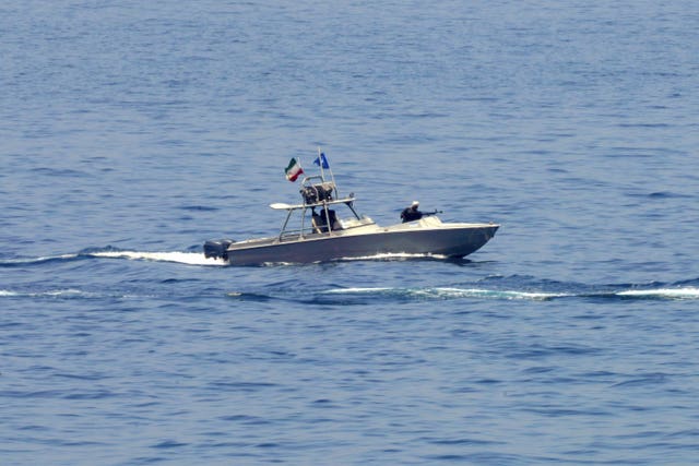 An Iranian Revolutionary Guard vessel watches an American warship in the Strait of Hormuz