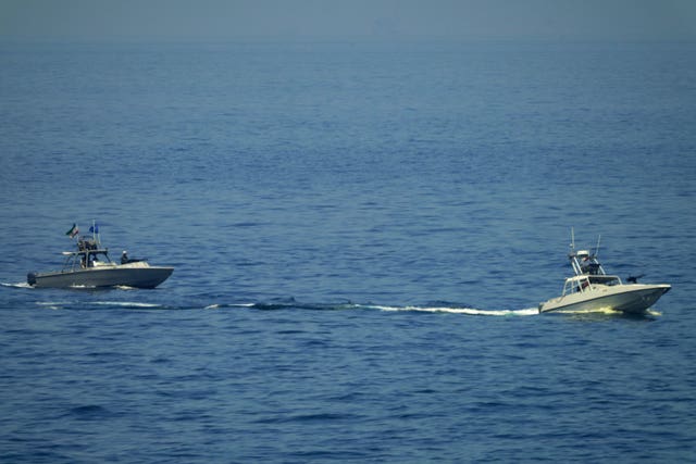 Iranian Revolutionary Guard vessels watch an American warship in the Strait of Hormuz 