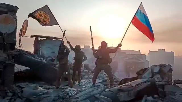 Yevgeny Prigozhin’s Wagner Group military company members wave a Russian national and Wagner flag atop a damaged building in Bakhmut, Ukraine 