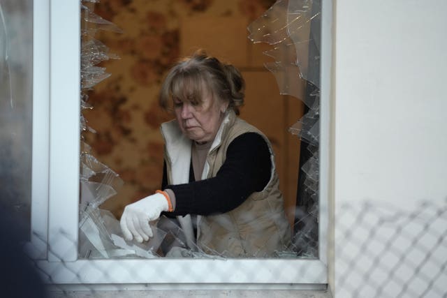 A woman clears broken glass from the window of a multi-storey apartment building damaged during a Russian attack on Kyiv