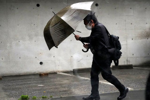 A person holds an umbrella against strong wind and rain on a street in Tokyo