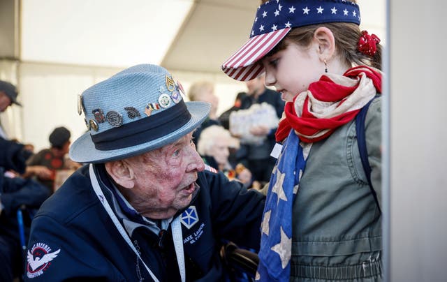 US veteran Jake M Larson talks to a girl wearing an American flag around her neck during a gathering in preparation of the 79th D-Day anniversary in La Fiere, Normandy, France