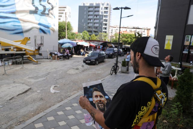 Argentinian street artist Maximiliano Bagnasco looks at a picture of Argentinian footballer Lionel Messi, in front of Messi’s mural that he is painting, in Tirana, Albania