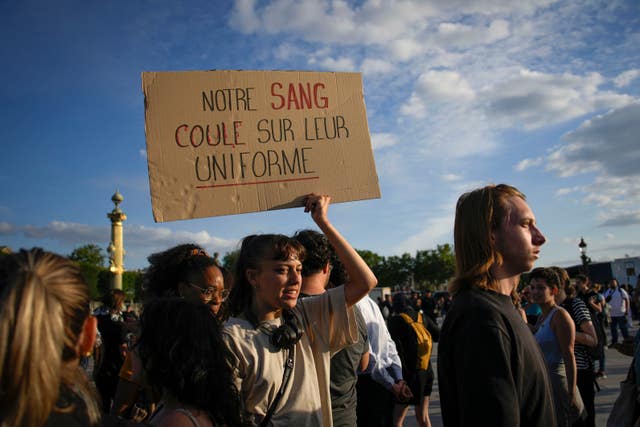 A woman holds a placard reading “Our blood runs on their uniform” during a protest in Paris