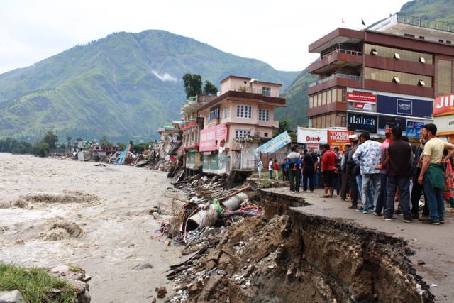 People stand by a road washed away by the River Beas swollen due to heavy rains in Kullu District, Himachal Pradesh, India