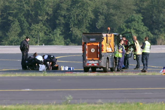 Police officers and security personnel stand on the airfield and try to detach activists of the group Last Generation who have stuck themselves to the asphalt in the airport area in Duesseldorf, Germany