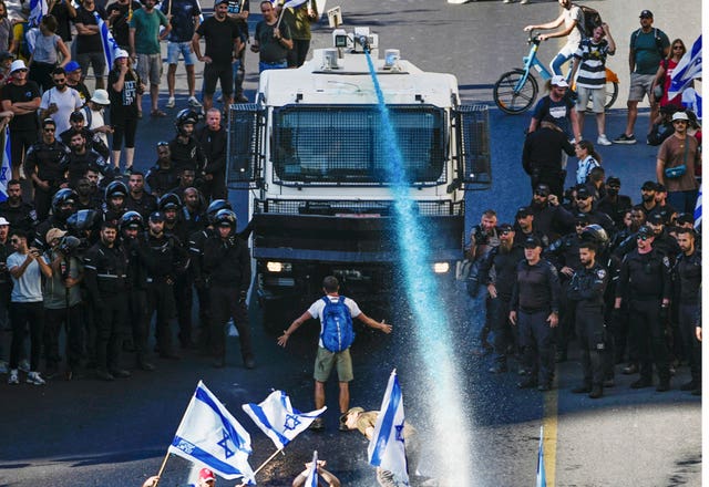 A person stands in front of an Israeli police water cannon being used to disperse demonstrators blocking a road in Jerusalem