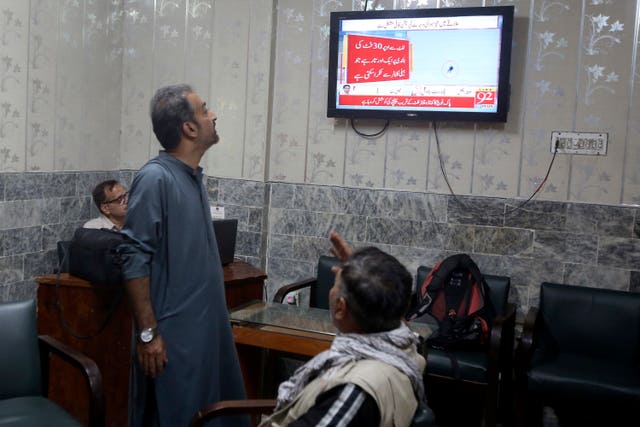 Members of the media watch a news channel airing live coverage of the people trapped in a cable car