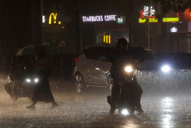 People walk and drive in heavy rain as Typhoon Haikui approached Taiwan on Saturday