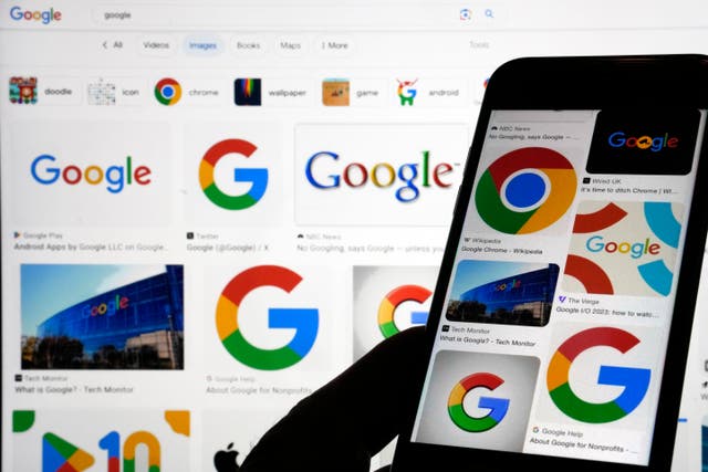 A laptop screen shows lots of Google logos and in front of it, someone is holding up a smartphone that also shows lots of google icons