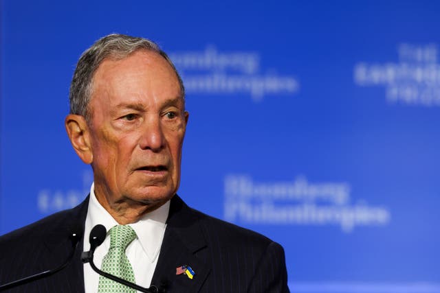 Michael Bloomberg in a suit, making a speech against a blue background