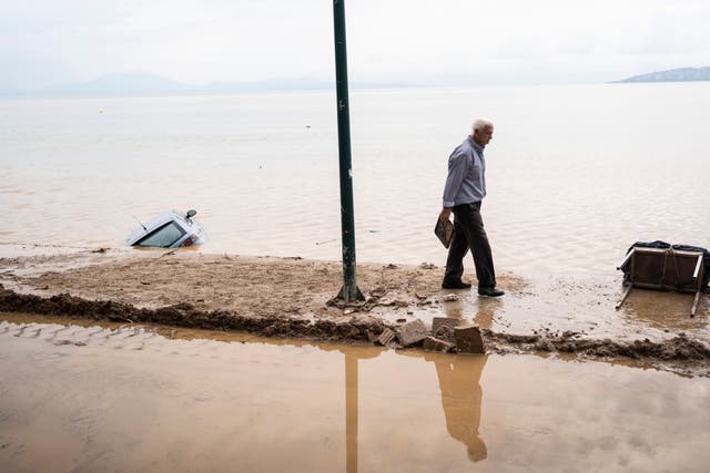 A man walks by the seaside, past a car washed away by flood water, in the town of Agria