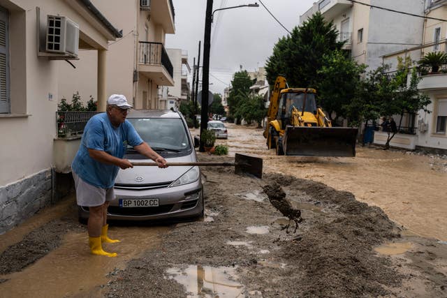 A man shovels mud outside his house in a flooded street in Volos
