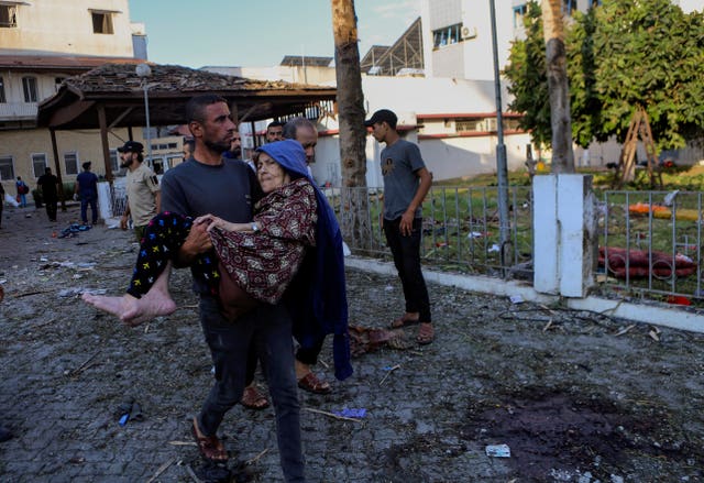 A Palestinian man carries an elderly woman past the site of a deadly explosion at al Ahli hospital