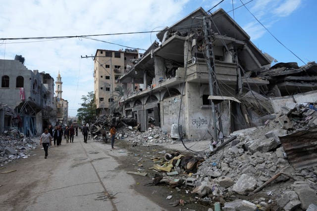 Palestinians walk past buildings destroyed in the Israeli bombardment of the Gaza Strip, at the main road in Bureij refugee camp, Gaza Strip 