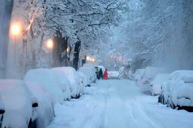 People remove a fallen tree from a road after heavy snowfall in Munich, Germany