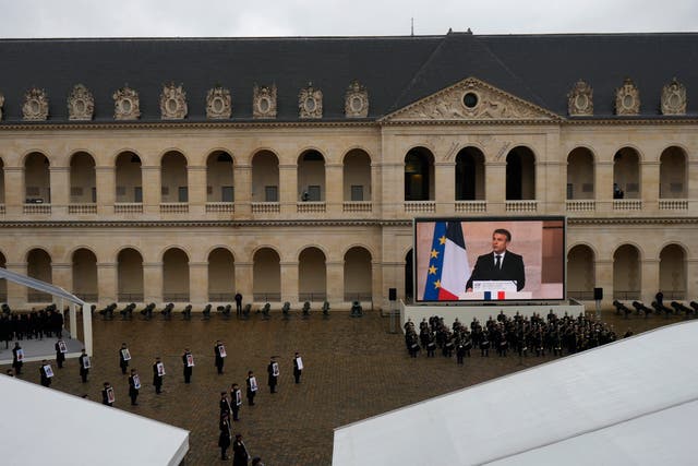 Photographs of the French victims of the Hamas October 7 2023 attack are displayed as French President Emmanuel Macron speaks, during a ceremony at the Invalides monument