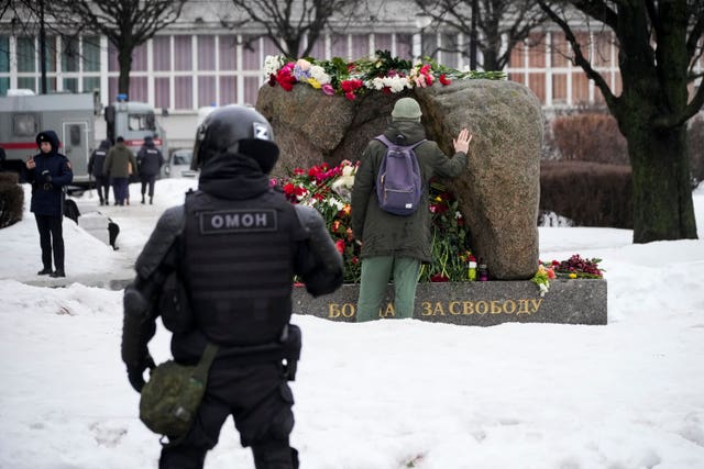 A police officer watches as a man lays flowers paying the last respects to Alexei Navalny at the monument where the first camp of the Gulag political prison system was established, in St Petersburg, Russia