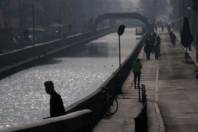 People walk along the Naviglio Pavese canal in Milan, Italy, shrouded in mist and smog 