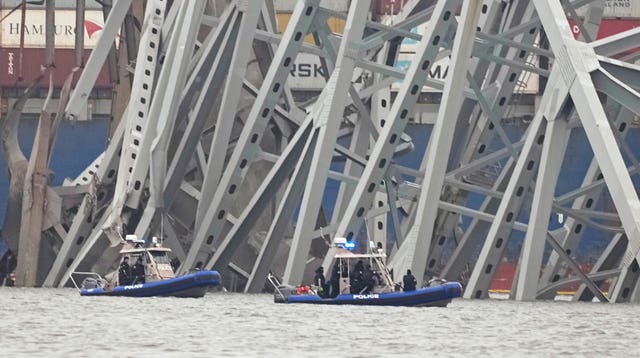 Police boats work around a cargo ship that is stuck under part of the structure of the Francis Scott Key Bridge in Baltimore