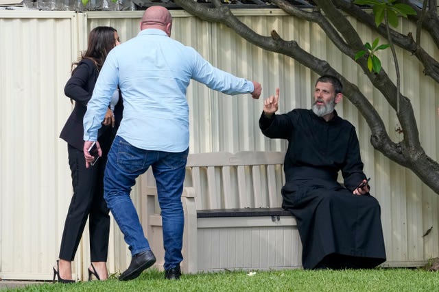 Father Daniel Kochou, right, gestures as he speaks with people, across the road from the Christ the Good Shepherd church in suburban Wakely in western Sydney 