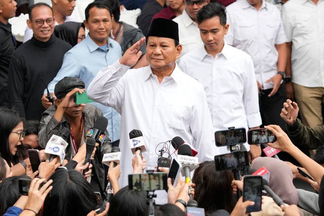 Indonesiam president-elect Prabowo Subianto salutes during a rally with supporters. He is surrounded by microphones and cameras as well as his backers.