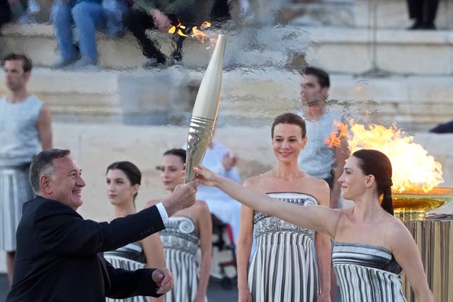 Actress Mary Mina, playing an ancient Greek high priestess, gives the torch with the Olympic Flame to the head of Greece’s Olympic Committee, Spyros Capralos, during the Olympic flame handover ceremony at Panathenaic stadium in Athens