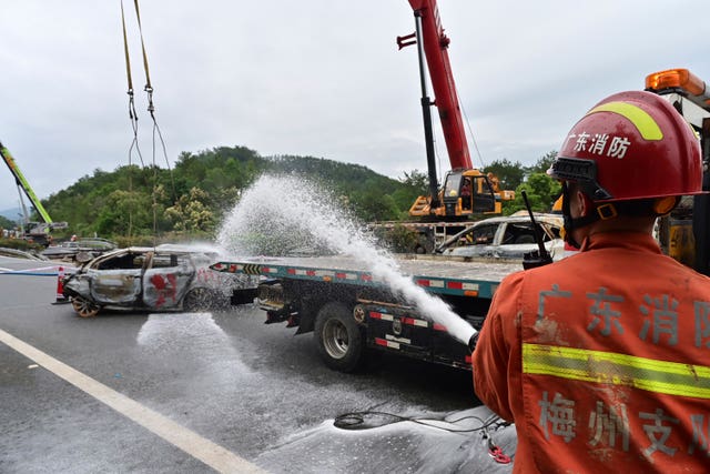 A firefighter sprays water on the remains of a car in the aftermath of the road collapse