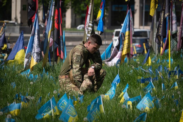 A Ukrainian soldier installs a small national flag on a grassed area at the Independence Square in Kyiv, Ukraine